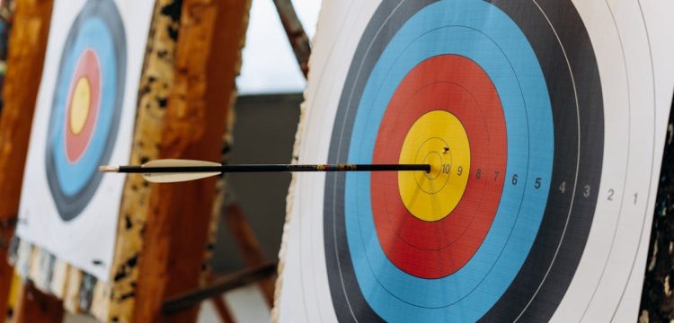 An arrow hits the bullseye on a colorful target in an indoor archery range.