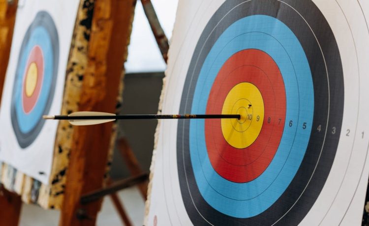 An arrow hits the bullseye on a colorful target in an indoor archery range.